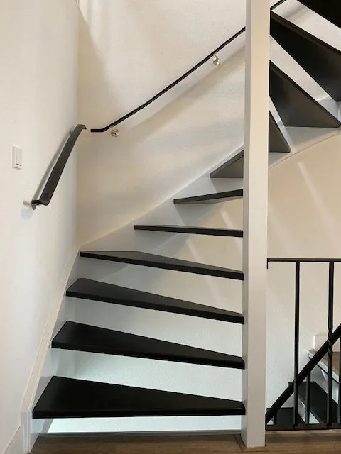 Trap met zwarte treden en leuning langs een witte wand