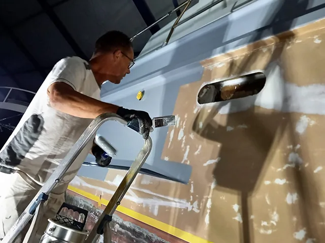 Schilder aan het werk aan de romp van een jacht in een loods