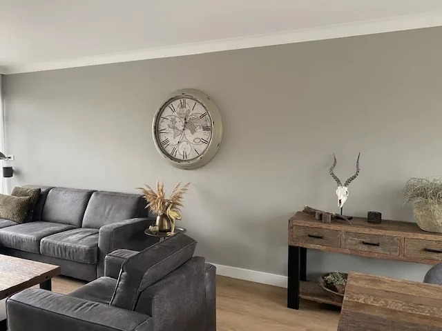 Woonkamer met grijze bank, wandklok en houten sidetable