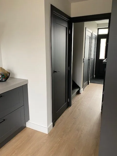 Gang met donkere deur, houten vloer en grijze kastjes