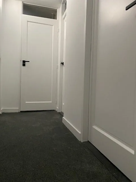 Smalle gang met witte deuren en een donkergrijze wand