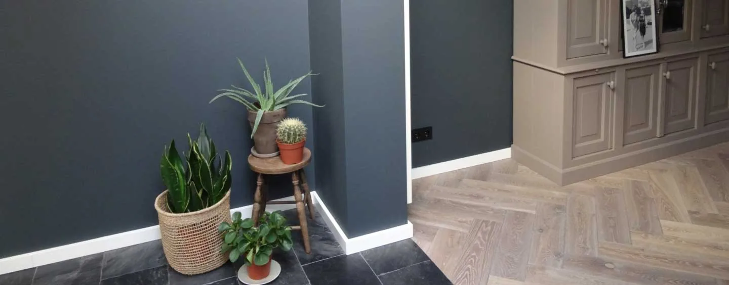 Grijze wand met visgraatparket, planten en een witte deur