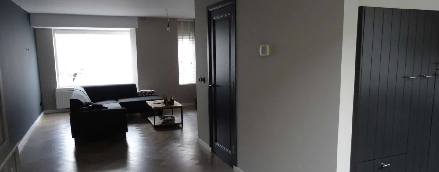Woonkamer met zwarte bank, donkere deur en lichte wand