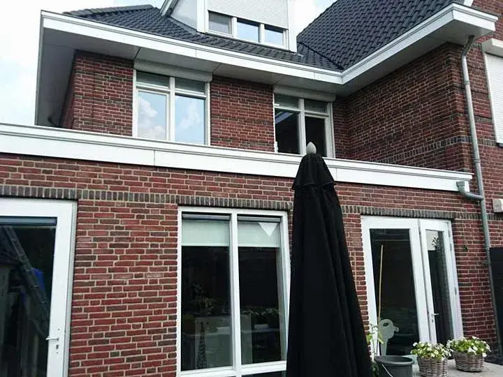 Rode baksteen gevel met witte kozijnen en een zwarte parasol